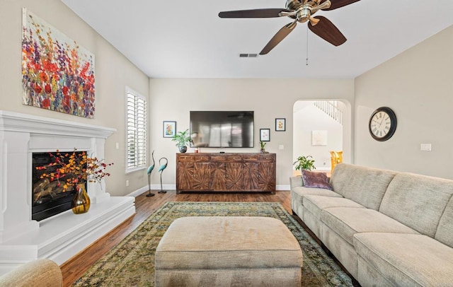 living area with a warm lit fireplace, visible vents, baseboards, and wood finished floors