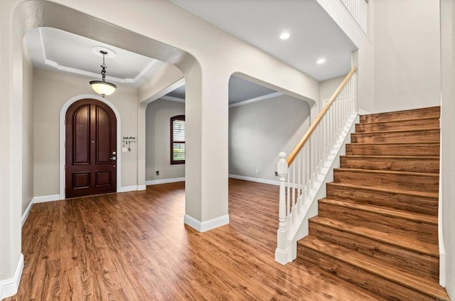 entrance foyer with arched walkways, wood finished floors, baseboards, stairs, and ornamental molding