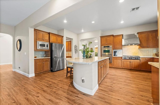 kitchen with visible vents, arched walkways, a center island, stainless steel appliances, and wall chimney range hood