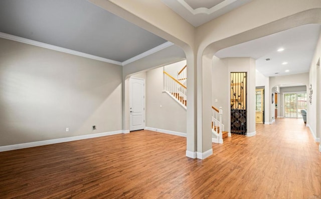 interior space featuring arched walkways, crown molding, wood finished floors, baseboards, and stairs