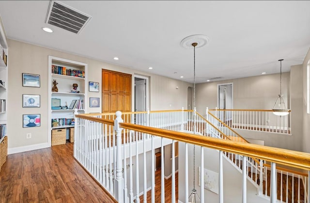 hallway featuring built in shelves, recessed lighting, visible vents, an upstairs landing, and wood finished floors