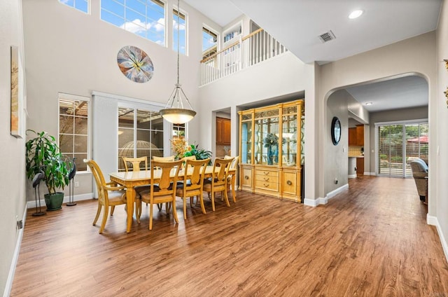 dining space featuring arched walkways, light wood finished floors, recessed lighting, visible vents, and baseboards