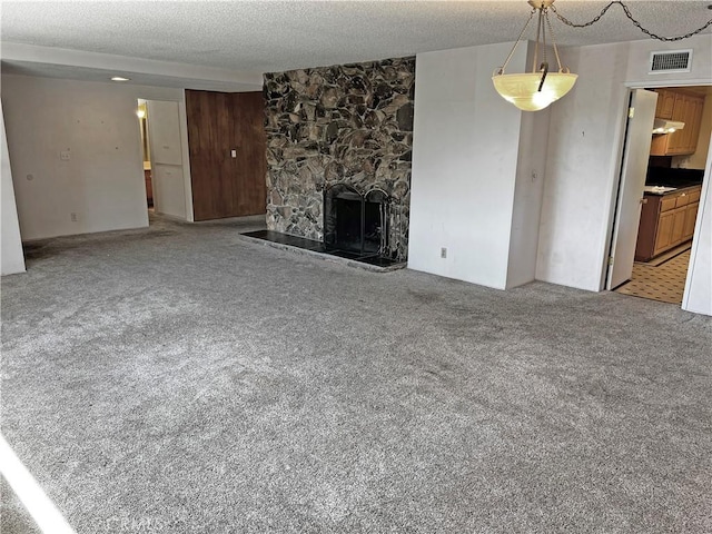 unfurnished living room with a textured ceiling, a stone fireplace, visible vents, and light colored carpet