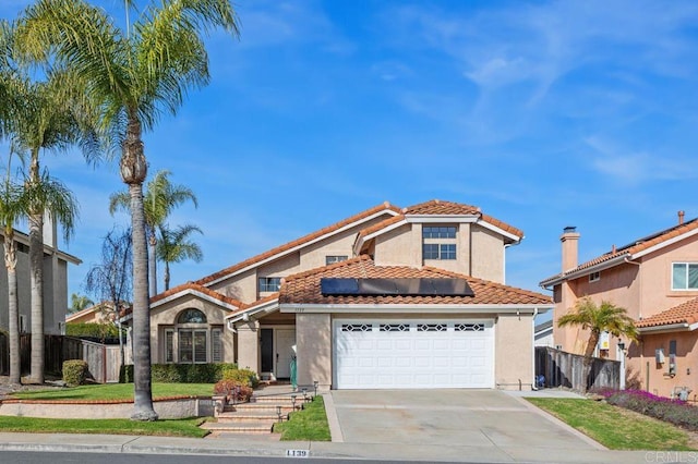 mediterranean / spanish-style home featuring stucco siding, concrete driveway, an attached garage, fence, and a tiled roof