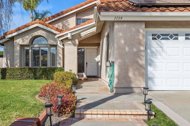 entrance to property featuring a garage, a tile roof, and stucco siding