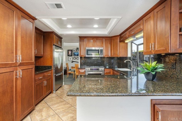 kitchen with stainless steel appliances, a raised ceiling, visible vents, dark stone counters, and a peninsula