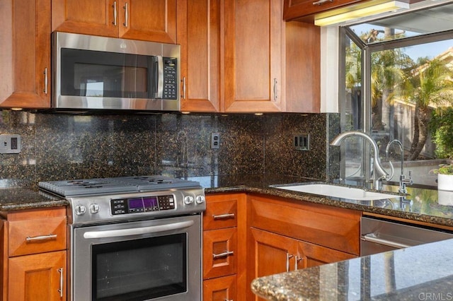 kitchen with brown cabinetry, decorative backsplash, dark stone counters, appliances with stainless steel finishes, and a sink