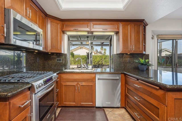 kitchen featuring appliances with stainless steel finishes, brown cabinetry, a sink, and dark stone countertops