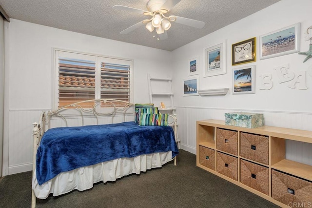 bedroom featuring a textured ceiling, dark colored carpet, and wainscoting