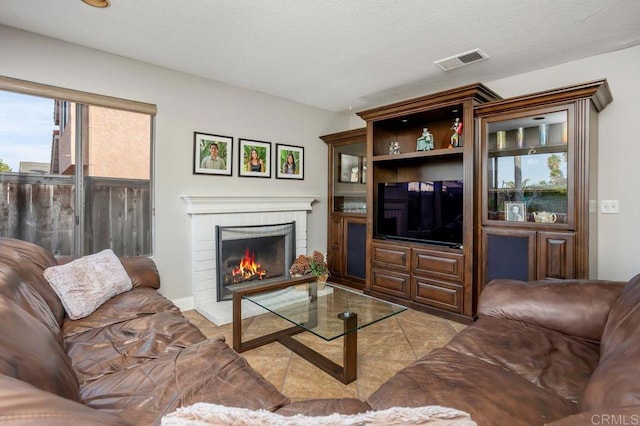 living area featuring a brick fireplace, light tile patterned floors, visible vents, and a textured ceiling