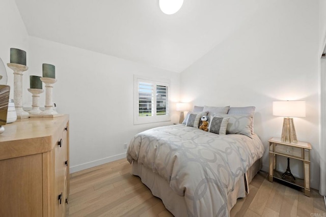 bedroom with light wood finished floors, baseboards, and vaulted ceiling