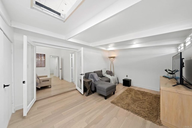 living area with a skylight, baseboards, beamed ceiling, and wood finished floors