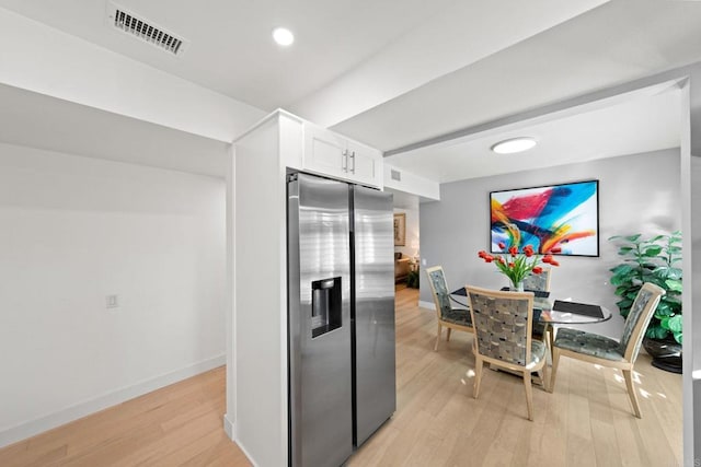 kitchen featuring stainless steel refrigerator with ice dispenser, visible vents, white cabinets, light wood-type flooring, and baseboards