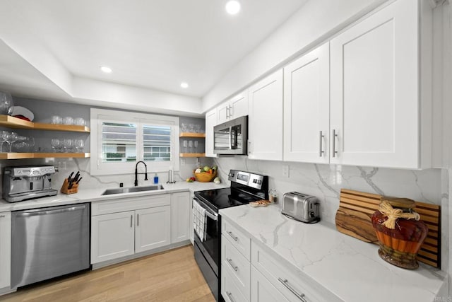 kitchen with light stone counters, appliances with stainless steel finishes, white cabinetry, open shelves, and a sink