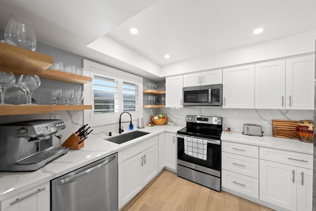 kitchen featuring open shelves, appliances with stainless steel finishes, white cabinets, a sink, and light stone countertops