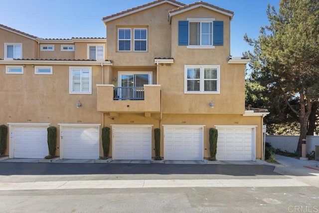 rear view of property featuring a tiled roof, an attached garage, and stucco siding