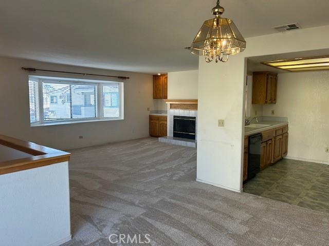 kitchen featuring visible vents, dishwasher, brown cabinets, light countertops, and dark carpet