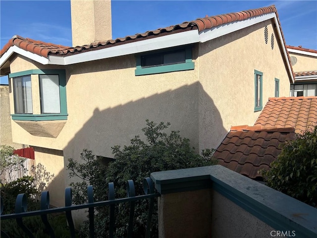 view of side of home with a chimney, fence, and stucco siding