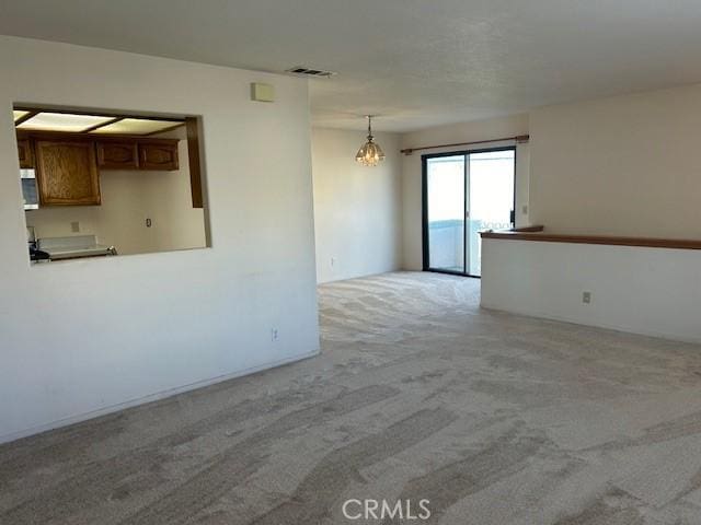 unfurnished living room with a chandelier, light colored carpet, and visible vents