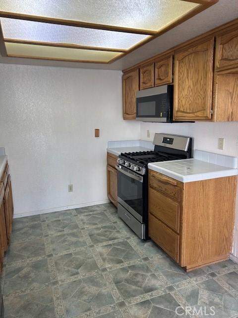 kitchen with stainless steel appliances, brown cabinetry, light countertops, and stone finish flooring