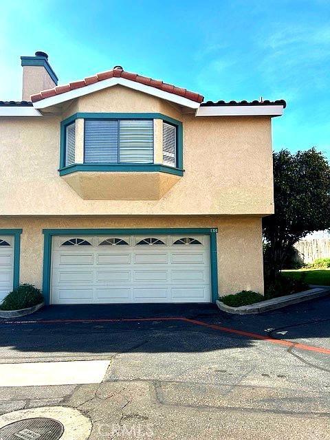 view of side of home featuring aphalt driveway, a chimney, an attached garage, and stucco siding