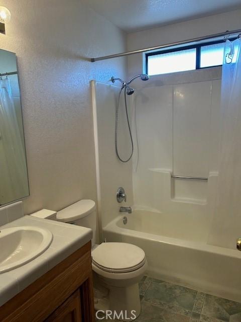 bathroom featuring a textured wall, shower / tub combo with curtain, vanity, and toilet