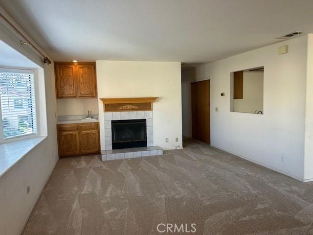 unfurnished living room with a fireplace, visible vents, a sink, and light colored carpet