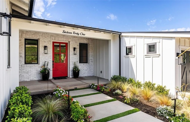 view of exterior entry featuring covered porch, board and batten siding, and brick siding