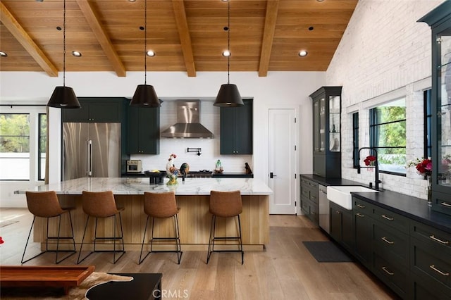 kitchen with a kitchen bar, hanging light fixtures, appliances with stainless steel finishes, glass insert cabinets, and wall chimney exhaust hood