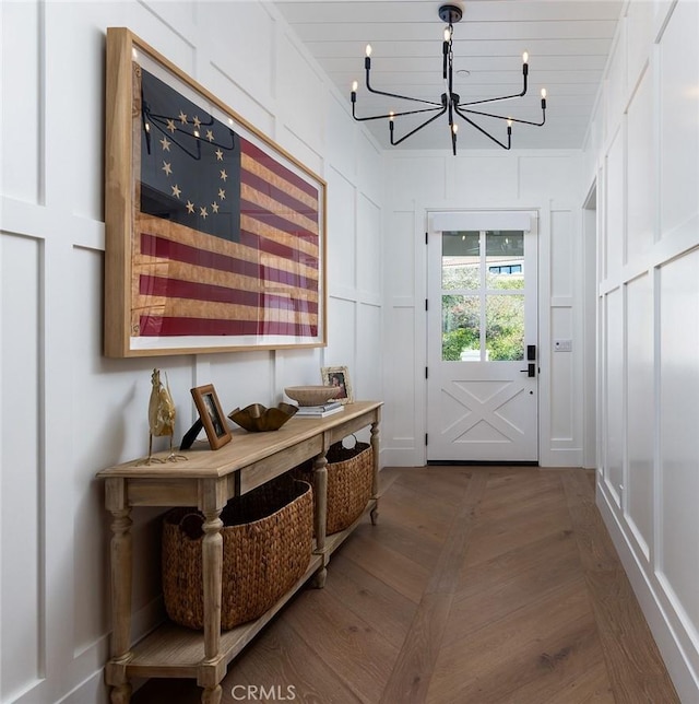 doorway to outside with wood finished floors, a decorative wall, and an inviting chandelier