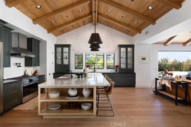 kitchen featuring stainless steel gas range, a kitchen island with sink, glass insert cabinets, and wall chimney exhaust hood