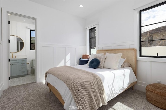 carpeted bedroom featuring ensuite bathroom, a decorative wall, a sink, and recessed lighting