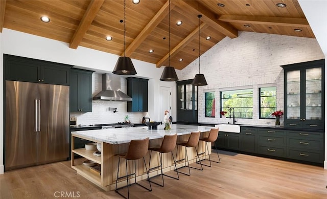 kitchen featuring a sink, wall chimney range hood, stainless steel fridge, and glass insert cabinets