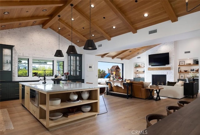 kitchen featuring light stone counters, a center island with sink, hanging light fixtures, glass insert cabinets, and wood ceiling