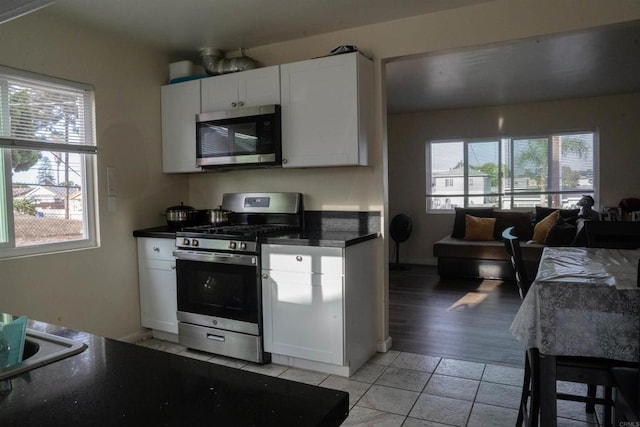 kitchen featuring appliances with stainless steel finishes, light tile patterned flooring, dark countertops, and white cabinetry