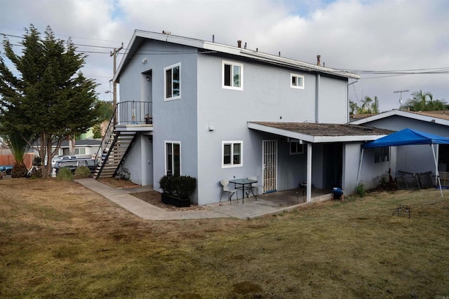 rear view of house with a patio area, stucco siding, a lawn, and stairs