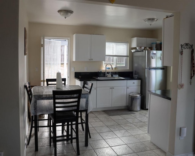 kitchen with light tile patterned floors, dark countertops, freestanding refrigerator, white cabinetry, and a sink