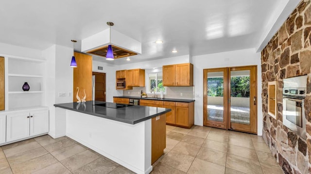 kitchen featuring brown cabinetry, dark countertops, a peninsula, hanging light fixtures, and stainless steel appliances