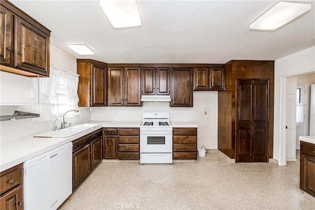 kitchen with dark brown cabinetry, under cabinet range hood, white appliances, a sink, and decorative backsplash