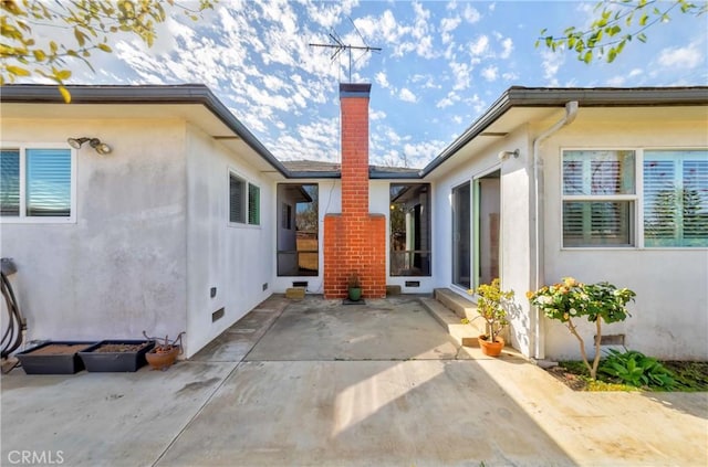 rear view of property with a chimney, a patio, and stucco siding