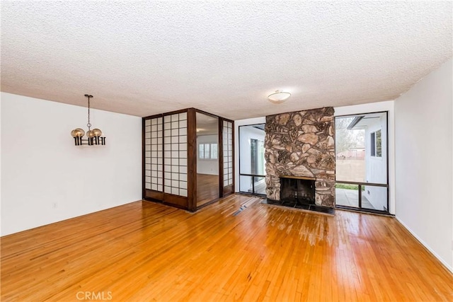 unfurnished living room with light wood-type flooring, a chandelier, a textured ceiling, and a stone fireplace