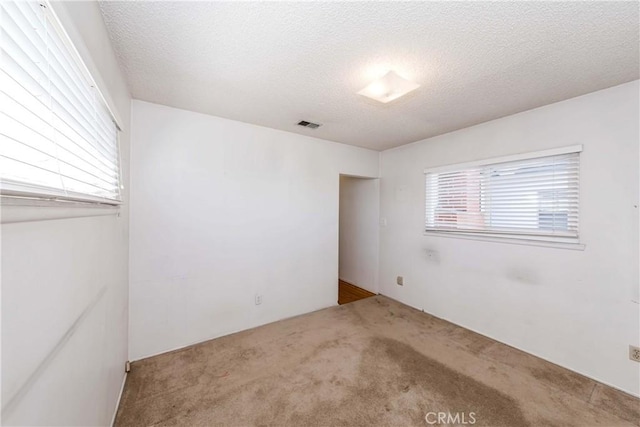 spare room featuring carpet, visible vents, and a textured ceiling