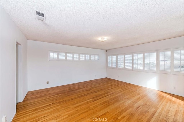 empty room featuring a wealth of natural light, visible vents, a textured ceiling, and light wood finished floors