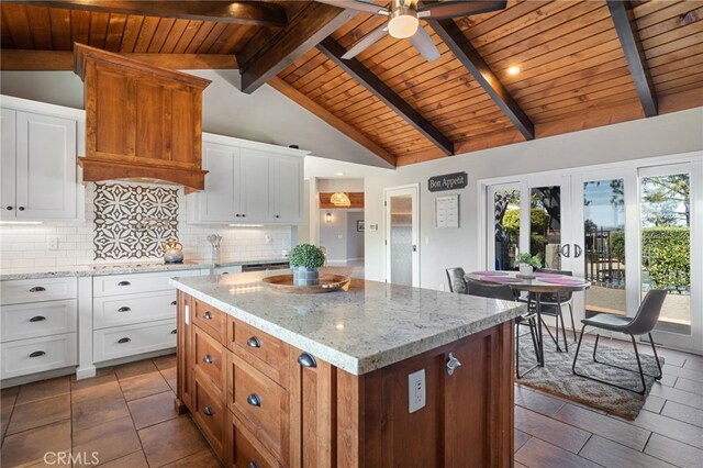 kitchen with tasteful backsplash, a center island, white cabinetry, light stone countertops, and vaulted ceiling with beams