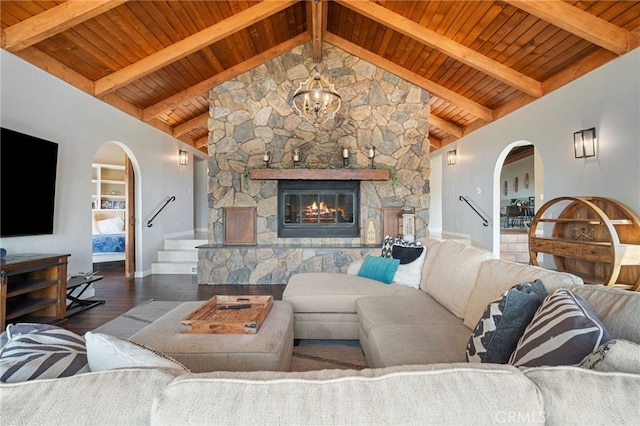 living area featuring wood finished floors, stairs, arched walkways, a stone fireplace, and vaulted ceiling with beams