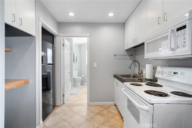 kitchen featuring baseboards, light tile patterned floors, white cabinets, white appliances, and a sink