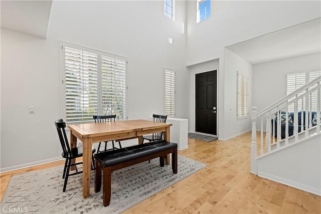 dining area with a towering ceiling, light wood-style floors, stairs, and baseboards