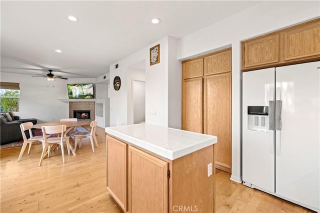 kitchen with tile countertops, a fireplace, open floor plan, white fridge with ice dispenser, and light wood finished floors