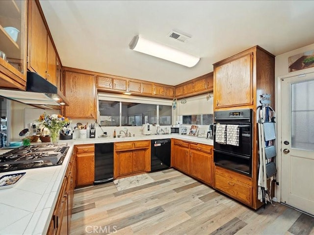 kitchen with a warming drawer, black appliances, under cabinet range hood, tile countertops, and brown cabinetry