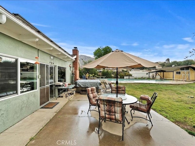 view of patio with a storage shed, an outdoor structure, outdoor dining space, and an outdoor pool